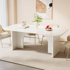 a white dining table with chairs around it and a bowl of fruit on the table