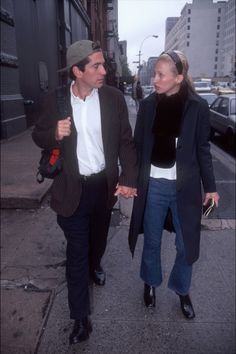 a man and woman walking down the street holding hands, both wearing black jackets and white shirts