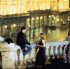 a man and woman standing on a balcony next to each other in front of a building