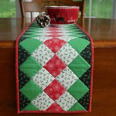 a table topped with a green and red quilted christmas table runner next to a potted plant