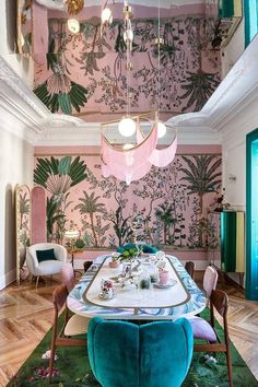 the dining room is decorated with pink and green wallpaper, gold chandeliers, and blue velvet chairs