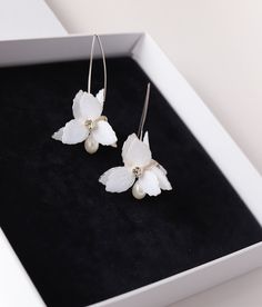 two white flowers with pearls on them are sitting in a black and white gift box