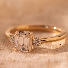 an engagement ring with three stones on top and one stone in the middle, sitting on a piece of cloth