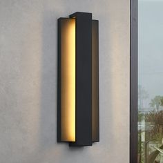 a wall mounted light on the side of a building with an open window behind it