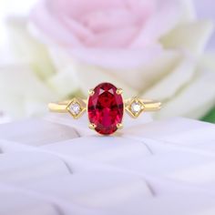 a red stone ring sitting on top of a white surface next to a pink rose