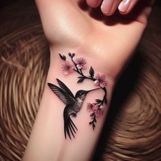 a small tattoo on the wrist of a woman's arm with flowers and a hummingbird