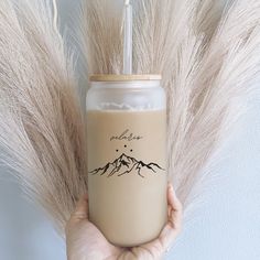 a person holding a drink in front of some dry grass with the words alaska written on it