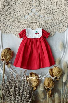 a red and white dress is hanging on the wall next to dried flowers