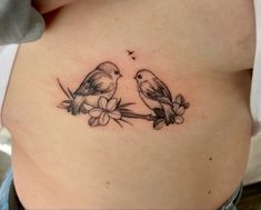 two birds sitting on a branch with flowers in the middle of their stomach tattoo design