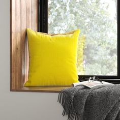 a yellow pillow sitting on top of a window sill next to a gray blanket