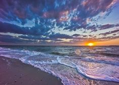 the sun is setting over the ocean with clouds in the sky and waves on the beach