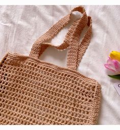 a crocheted bag sitting on top of a bed next to a pink flower