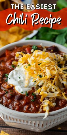 a bowl filled with chili and cheese next to tortilla chips on the side