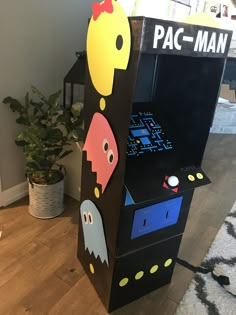 an arcade machine with pac - man and ghost faces on it's side, next to a potted plant