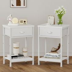 two white nightstands side by side with flowers and books on them in a living room