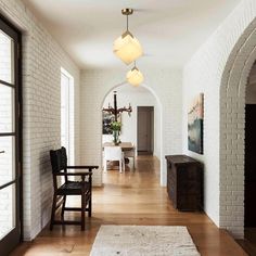 a long hallway with white brick walls and wooden flooring, along with an arched doorway leading to the dining room