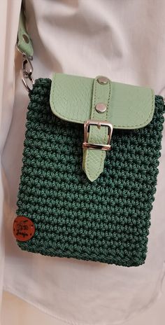 a green crocheted bag with a metal buckle on the front and side, attached to a woman's white shirt