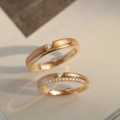 two gold wedding rings with diamonds on top of each other, sitting on a white surface