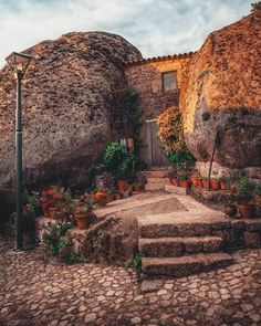 an old stone house with potted plants on the steps and stairs leading up to it