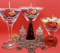 three wine glasses with candles in them on a pink background, decorated with flowers and beads