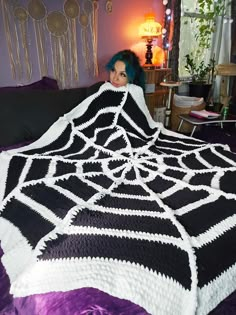 a woman with blue hair laying in bed under a black and white crocheted blanket