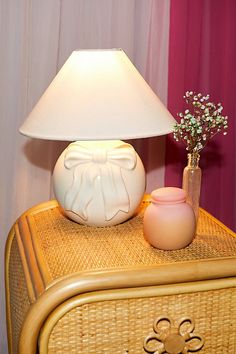 a lamp on top of a wicker dresser next to a vase with baby's breath