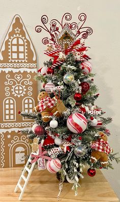 a small christmas tree with ornaments on it and a gingerbread house in the background