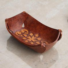 a wooden bowl sitting on top of a floor next to a vase with flowers in it