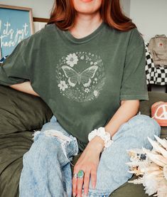 In this wildflower butterfly tee, a graceful silhouette flutters amidst a vibrant arrangement of blooms, inviting you to immerse yourself in nature's beauty. Let this charming design elevate your spirit with every wear. ★ Fabric ★ The Comfort Colors 1717 tee is made with medium fabric (6.1 oz/yd² (206.8 g/m consisting of high quality, 100% ring-spun US cotton for long-lasting comfort. Made using 100% US cotton that is ethically grown and harvested. ★ Fit ★ The relaxed fit keeps the wearer comfy in both casual and semi-formal settings while the crew neckline delivers that classic, neat style which makes it perfect for accessorizing.  The pre-shrunk fabric ensures a consistently great fit. ★ Care Instructions ★ ● Machine wash at a low heat. ● Wash garments inside-out, with similar colours. ● Casual Green Top With Butterfly Print, Fairycore Short Sleeve Tops For Spring, Green Butterfly Sleeve Tops For Spring, Summer Fairycore Top With Graphic Print, Cotton Tops With Floral Print And Butterfly Sleeves, Spring Fairycore Cotton Tops, Green Fairycore Tops For Summer, Spring Crew Neck Top With Butterfly Print, Green Fairycore Top For Summer