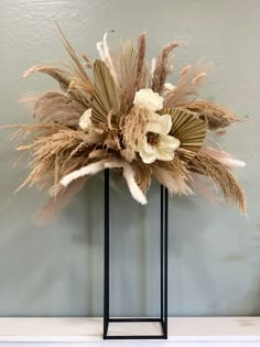 an arrangement of dried flowers and feathers on a stand