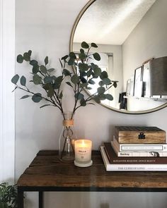 a mirror and some books on a table with a vase filled with flowers next to it