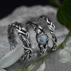 two silver rings sitting next to each other on top of a rock with flowers in the background