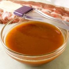 a glass bowl filled with sauce sitting on top of a counter next to a piece of meat