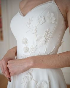 a woman in a white wedding dress is holding her hand on the back of her dress