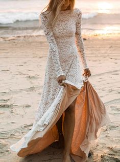 a woman is walking on the beach with her dress blowing in the wind and holding a bag