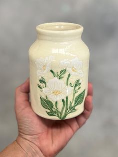 a hand holding a white vase with flowers painted on it