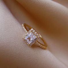 an engagement ring with a square cut diamond surrounded by small round diamonds on a beige cloth