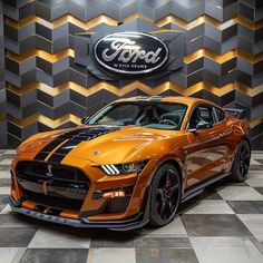 an orange sports car parked in front of a wall with the ford logo on it