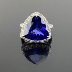 A beautiful Trillion Cut Cocktail Ring featuring a 12.54 Carat Tanzanite and 0.69 Carats of Diamond Accents set in White Gold. The centre stone Tanzanite is completely transparent, with no inclusions, and the gemstones are all set in 8 grams of 18K solid White Gold. All of our gemstones are 100% natural, certificate can be provided for authenticity. Please feel free to message us for more information, the ring comes with a certificate from an independent gem lab.  18K White Gold : 7.31 Grams  Tanzanite : 12.54 Ctw Diamond : 0.69 Ctw Luxury Trillion Cut Cubic Zirconia Jewelry, Luxury Blue Trillion Cut Jewelry, Luxury Sapphire Ring With Trillion-cut Diamond, Trillion Cut Cocktail Ring, Trillion Cocktail Ring, Luxury Cubic Zirconia Jewelry In Trillion Cut, Luxury Trillion Cut Sapphire Jewelry, Trillion Cut Diamond Ring, Natural Emerald Rings