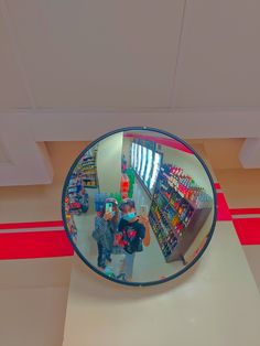 the reflection of two people standing in front of a store's large round mirror