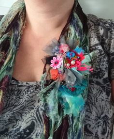 a woman wearing a scarf with flowers on it and a flower brooch attached to her neck