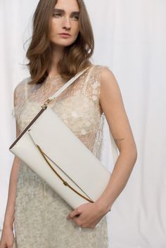 A white, elongated bag to be worn on the shoulder or for clutch-style carrying. Inside, there is an open compartment finished with viscose lining and a flat, elongated pocket on the back side of the bag that can be zipped shut. The clasp is handmade from brass according to our original design. The sides of the bag are made of pine wood, veneered with American walnut. There is an embossed logo on the front. Dimensions: 40 x 18 x 3 cm Included strap: 68 x 2 cm The body of the bag is made of the hi Cream Rectangular Shoulder Bag For Evening, Cream Rectangular Shoulder Bag For Evenings, Elegant Handheld Baguette Bag, Cream Rectangular Shoulder Bag For Formal Occasions, White Classic Rectangular Case Bag, Classic White Rectangular Case Bag, White Elegant Evening Bag For Travel, Formal Cream Rectangular Shoulder Bag, Elegant White Evening Bag For Travel