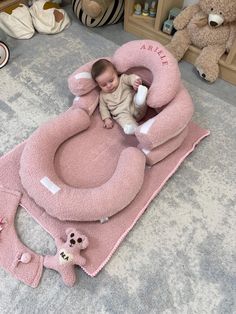 a baby is laying in a pink animal shaped bed on the floor next to stuffed animals