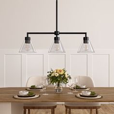 a dining room table with four lights hanging over it and place settings on the table