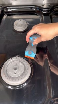 a person using a brush to clean an oven burner with a blue and black handle