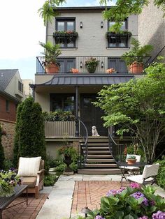 an outdoor patio with chairs and potted plants in front of a house that has stairs leading up to the second floor