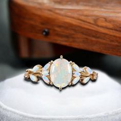 an opal and diamond ring sits on a white display stand in front of a wooden chair