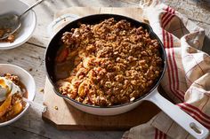 a pan filled with food sitting on top of a wooden table next to bowls and utensils