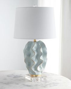 a white lamp sitting on top of a marble table next to a window with curtains