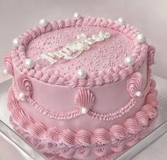 a pink birthday cake with pearls on the top and name written in white frosting